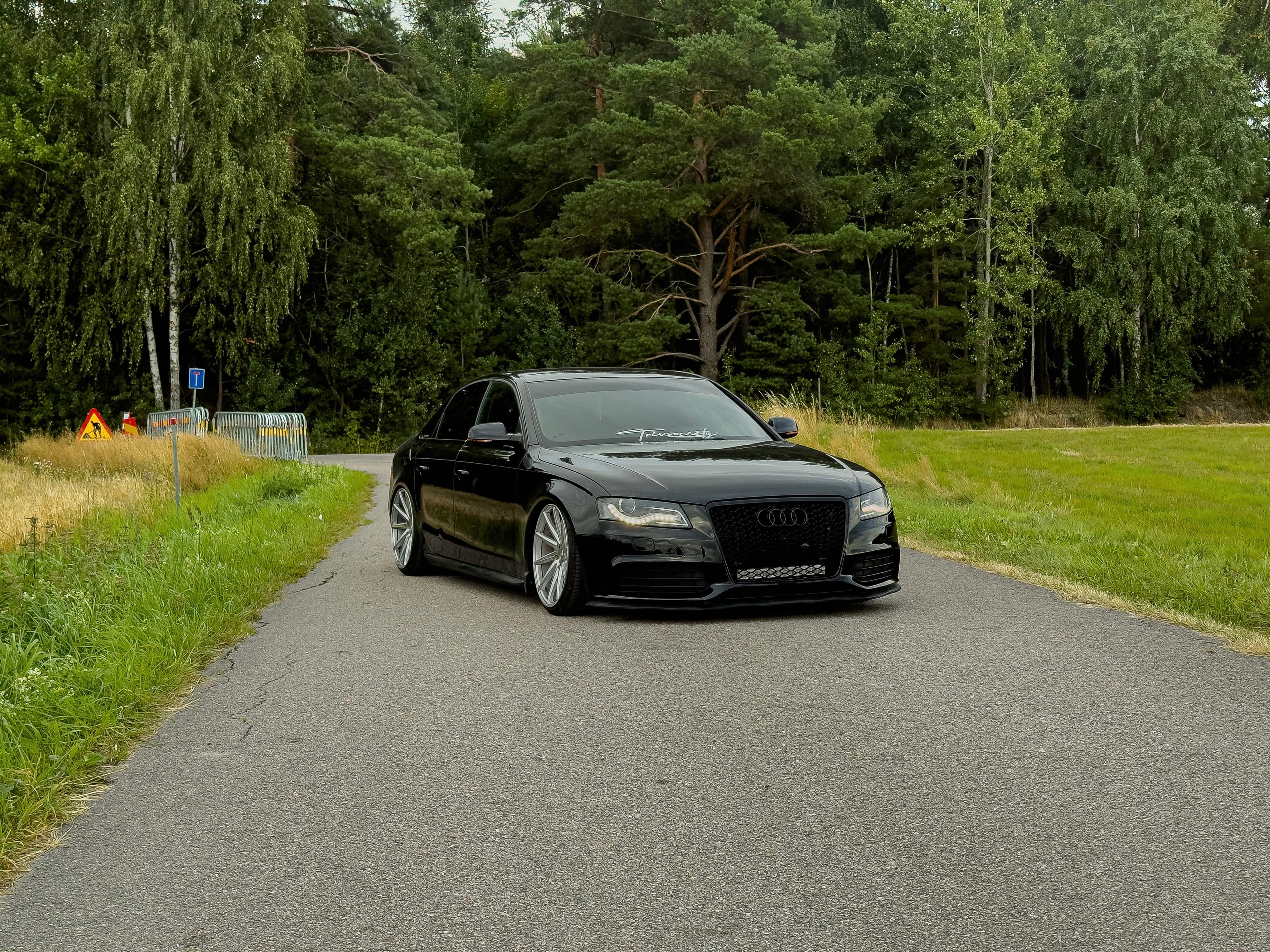 Svart Audi på en väg framför grönskande skog